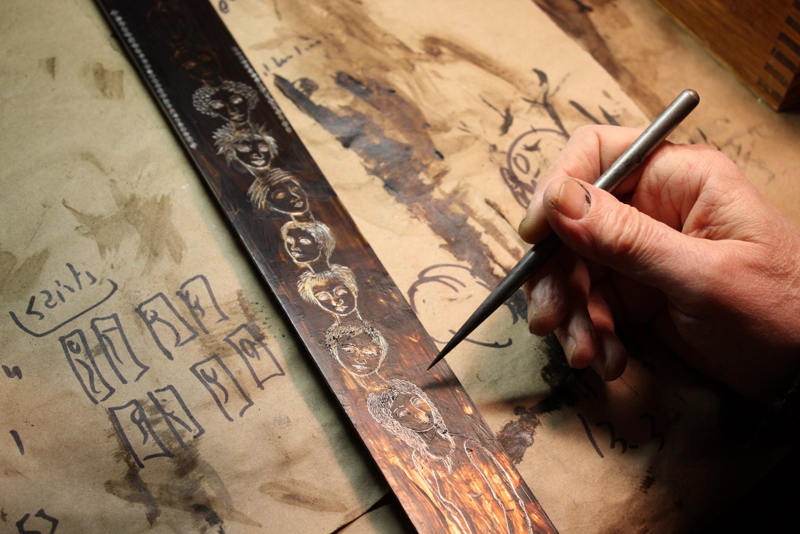 A close-up of Bert’s hand carefully engraving a line of faces into a copper plate