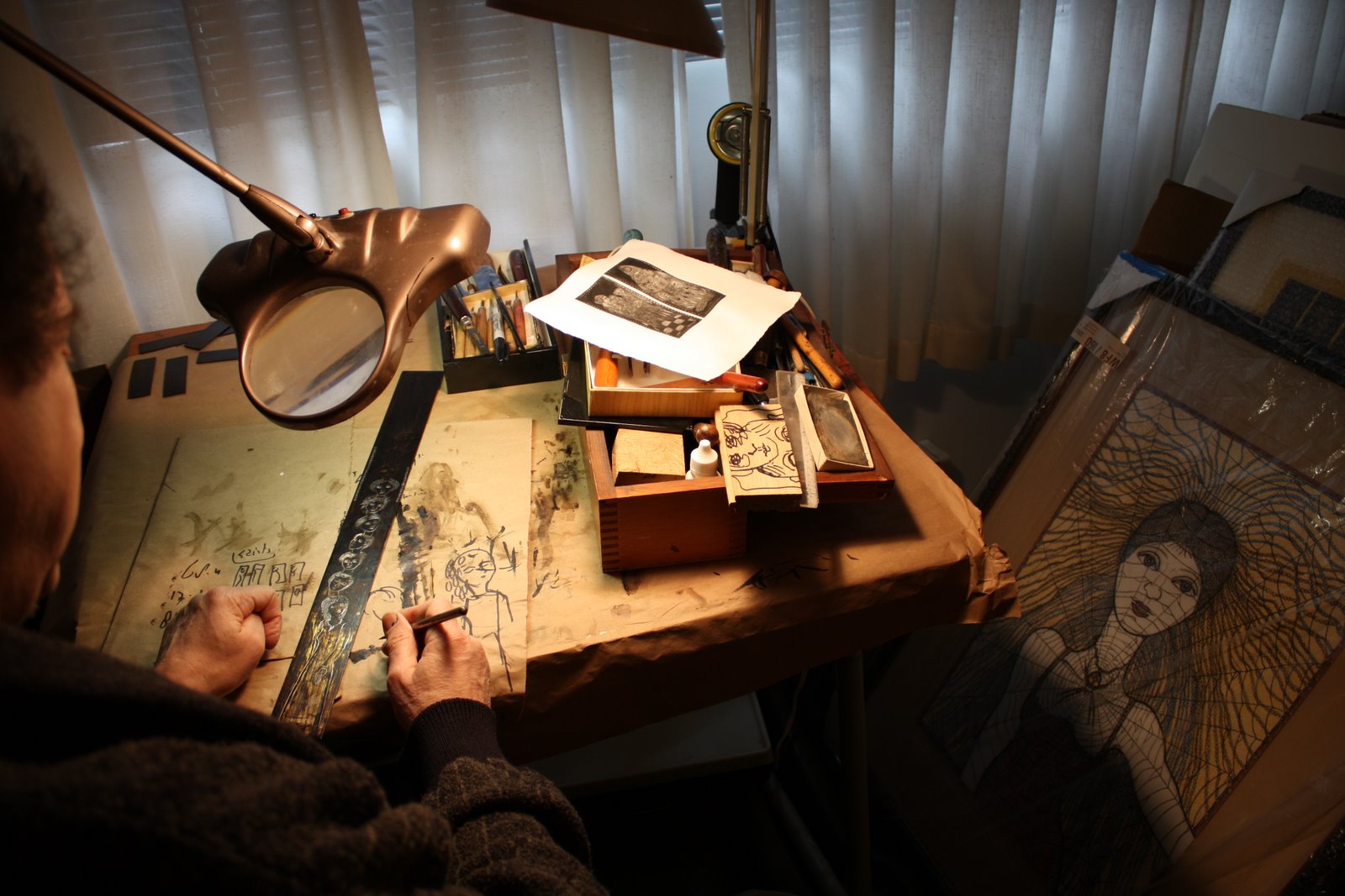 Bert Menco drawing at his worktable beneath a magnifying lamp